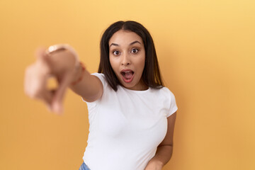 Young arab woman wearing casual white t shirt over yellow background pointing with finger surprised...