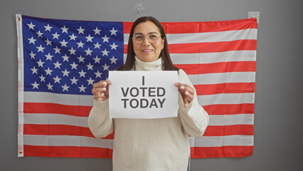 Middle-aged hispanic woman holds 'i voted today' sign before american flag, portraying civic duty...