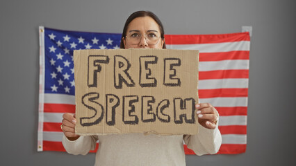 Hispanic woman holding a free speech sign in front of an american flag indoors.