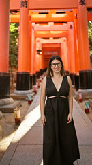 Gorgeous hispanic woman in glasses flaunting a radiant smile at the majestic torii gates of fushimi inari-taisha, kyoto