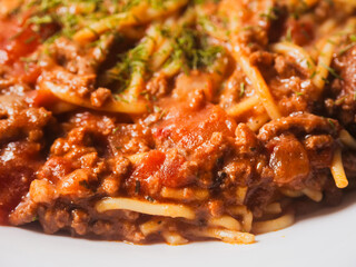 Spaghetti Bolognese serving on a white dish. Premium high quality meal with pasta, minced meat and tomato sauce. Top ingredients and herbs. Close up details shot. Light and airy look.