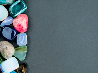 Colorful gems of different size and shape on a dark empty background for message. Design mock up. Natural materials decoration.