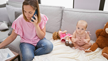Mother talking on smartphone reading document while daughter play with dolls on sofa at home
