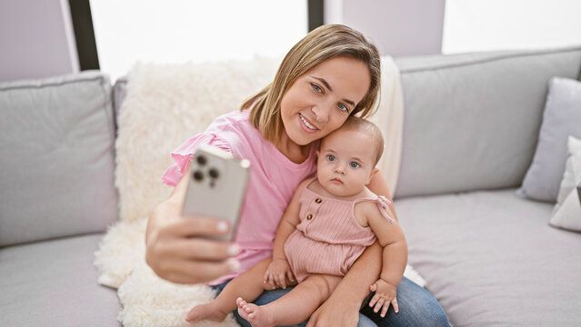 Cool mother and adorable daughter taking cozy sofa selfie, enjoying a casual, happy lifestyle at home, smiling with love and confidence