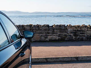 Side of a dark car parked with view on beautiful nature scene with ocean and mountains in...