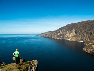 Man enjoys amazing view on Slieve league cliff standing on a edge of a rock. Travel and tourism...