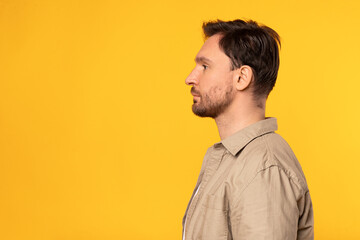 Obraz premium A man is standing in front of a bright yellow background. He is dressed casually and appears to be looking straight ahead, profile view