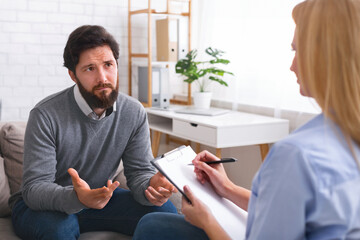 Psychotherapy. Unhappy depressed man speaking about his problems at personal consultation, free...