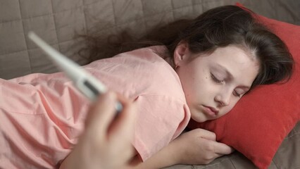 Worried mother taking child temperature. A worried mother check the daughter temperature laying on the sofa. A concept of feel virus infection during childhood.