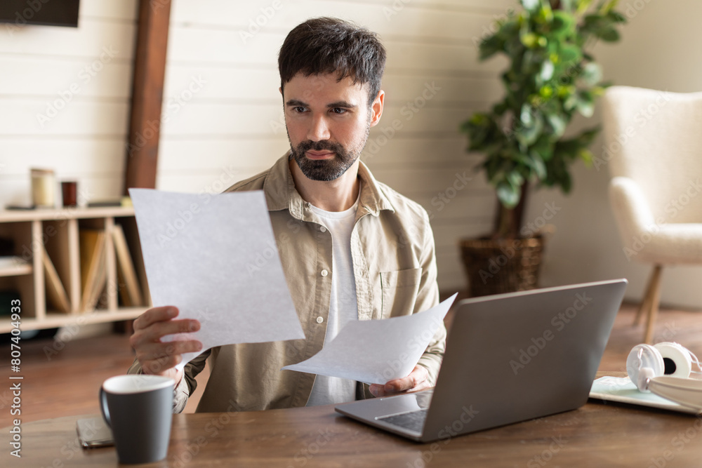 Poster a man is seated at a table, working on a laptop and surrounded by papers. he appears focused and eng