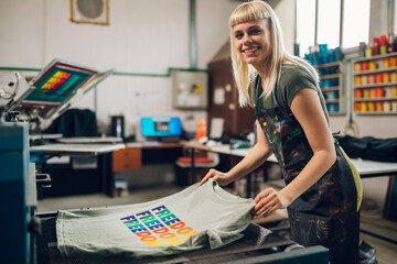 Happy print shop worker putting screen printed t-shirt in drying machine