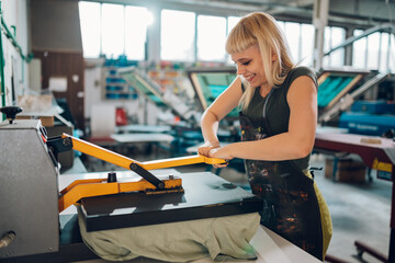 Smiling print shop worker using heating press on textile product.