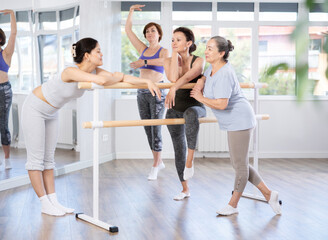 Group of cheerful relaxed women of different ages casually socializing and stretching beside ballet...