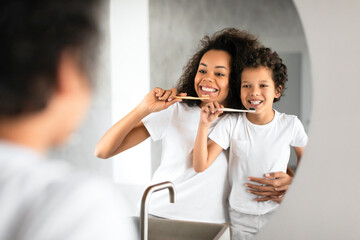 African American woman is standing next to a child, brushing her teeth with a toothbrush in a...