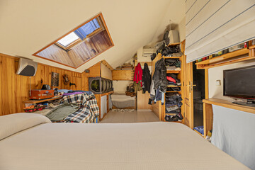 attic bedroom with skylight in the ceiling and wooden tongue-and-groove walls, matching shelves and...