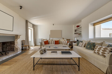 A large living room with a fireplace with large beige fabric sofas, wooden floors, natural fiber carpet and beautiful contemporary decoration