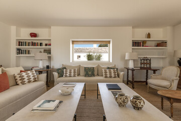 A large living room with a fireplace with large beige fabric sofas, wooden floors, natural fiber carpet, white coffee tables and beautiful contemporary decoration