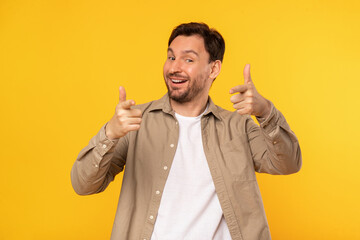 A cheerful man stands against a vivid yellow backdrop, giving a double thumbs up gesture while...