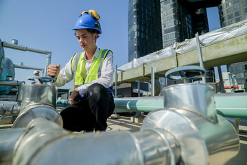 engineer inspecting HVAC equipment with a tablet on a building rooftop. An engineer attentively checks pipework on a rooftop against a cityscape, using a tablet for data analysis in urban maintenance.