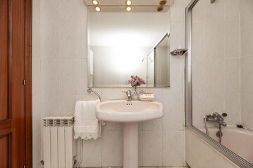 An old style toilet with white toilets with a porcelain sink under a beveled mirror with a shower cubicle with aluminum screens and mirror
