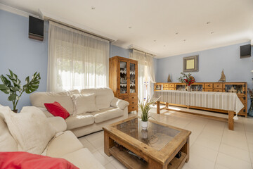 A living room with a large wooden dining table with matching shelves, blue walls and fabric...