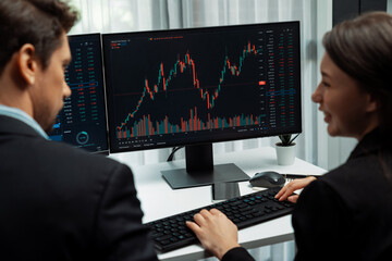 Two business traders discussing on dynamic stock market in currency rate investment trading on two pc screens with compare real time graph on risk or profit point of data at modern office. Postulate.