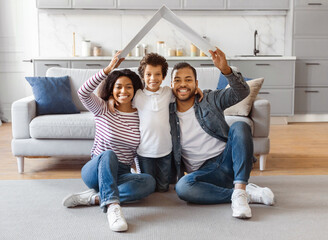 African American family seated on the floor facing a couch. They appear to be engaged in...