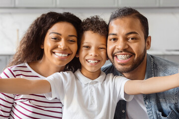 African American man, woman, and child are smiling and posing together while taking a selfie. They...