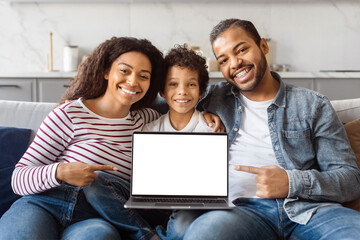 African American family sitting side by side on a couch, focused on a laptop screen in front of...