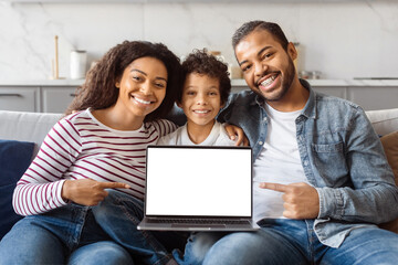 African American family sitting side by side on a couch, focused on a laptop screen in front of them, showing nice website for entertainment, copy space