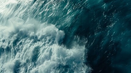 Fototapeta premium A birds eye view of the ocean waves crashing against the shore, creating foam and spray as they move towards the land.