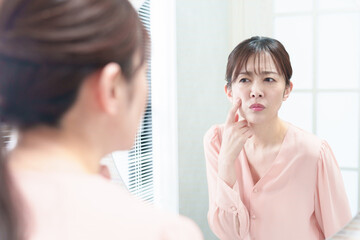 洗面台で鏡を見る女性　肌荒れ　お肌のトラブルイメージ