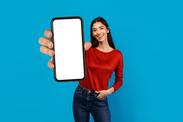 A woman wearing a red shirt is holding up a cell phone with blank screen in her hand, the screen is...