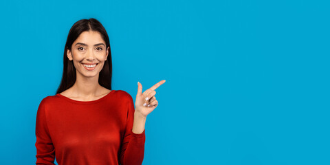 A cheerful woman with long hair wearing a red blouse stands against a vibrant blue backdrop. She...