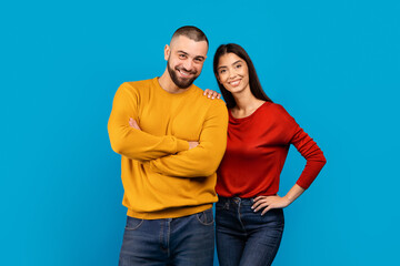 A man and woman standing together, smiling, and posing in front of the camera. They are dressed in...