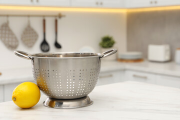 Empty colander and fresh lemon on white marble table in kitchen. Space for text