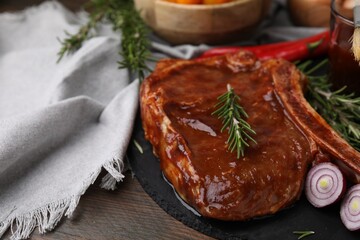 Tasty marinated meat, rosemary and onion on wooden table, closeup