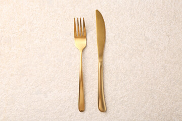 Elegant cutlery. Golden knife and fork on light textured table, top view