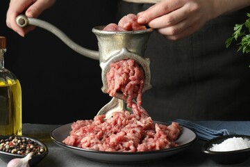 Woman making beef mince with manual meat grinder at grey table, closeup
