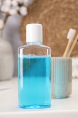 Bottle of mouthwash and toothbrushes on white table in bathroom