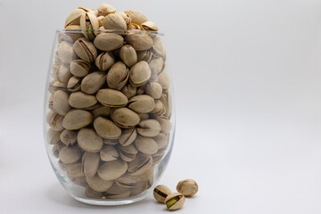 Pistachio nuts in a glass with three outside of glass on a white background
