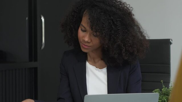 A young African American woman in a blue formal shirt with afro brown hair works as a product designer in a modern office, utilizing skills in design, CAD, CNC, and CNF.