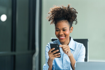 Attractive young African American woman, wearing a blue formal shirt and sporting afro brown hair, conducts market research as an analyst in a modern office using mobile technology.