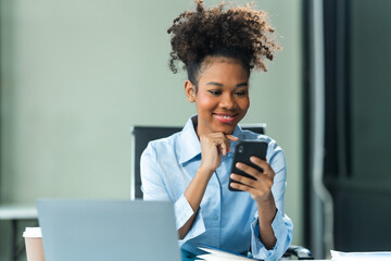 Attractive young African American woman, wearing a blue formal shirt and sporting afro brown hair, conducts market research as an analyst in a modern office using mobile technology.