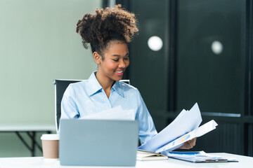 Analyzing business charts A4, a young African American woman in a blue formal shirt and afro brown...