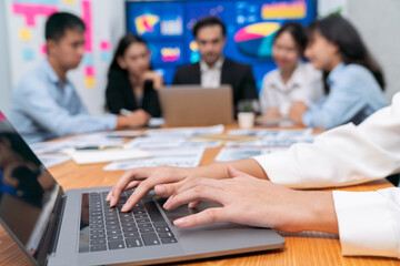 Closeup hand typing keyboard laptop with blurred background of business people using laptop to analyze financial data or data analysis display on screen background. Meticulous