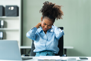 A young African American woman in a blue formal shirt with afro brown hair, suffering from office...