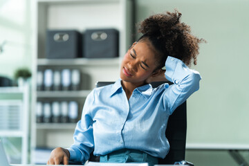 A young African American woman in a blue formal shirt with afro brown hair, suffering from office syndrome, navigates the challenges of being a businesswoman in a modern office.