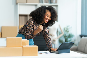 A young African American woman with afro brown hair works in a modern office, managing her online...