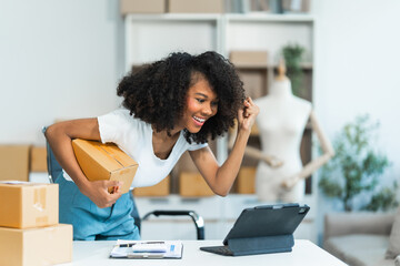 A young African American woman with afro brown hair works in a modern office, managing her online clothing store and live stream platform, sme box packages.